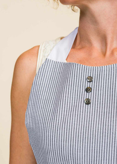 closeup of the neck of a woman wearing a black and white seersucker apron with three black buttons over the sternum