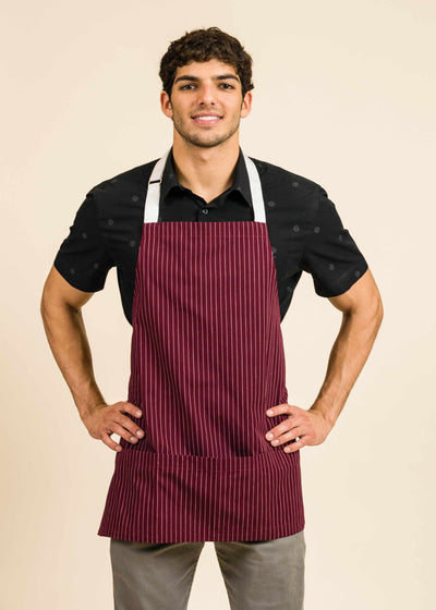 Athletic young man wearing a dark shirt, red apron with white stripes and white straps, and smiling at the camera