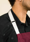 closeup of a white apron strap on a man's shoulder, showing the corner of the apron and the man's neck with stubble
