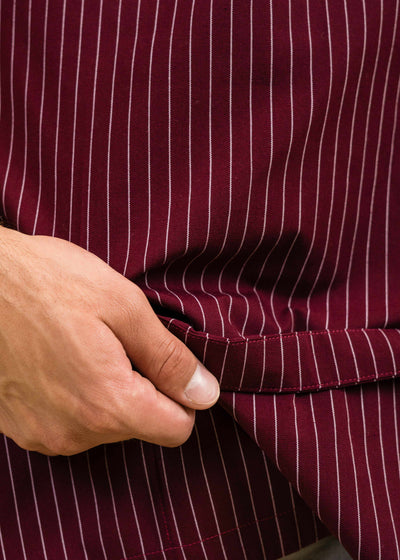 closeup of a hand showing the interior lining of a pocket on a dark red apron with white stripes