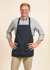 Handsome cook wearing his black apron with white stripes by jem, the Mel Short Full apron.